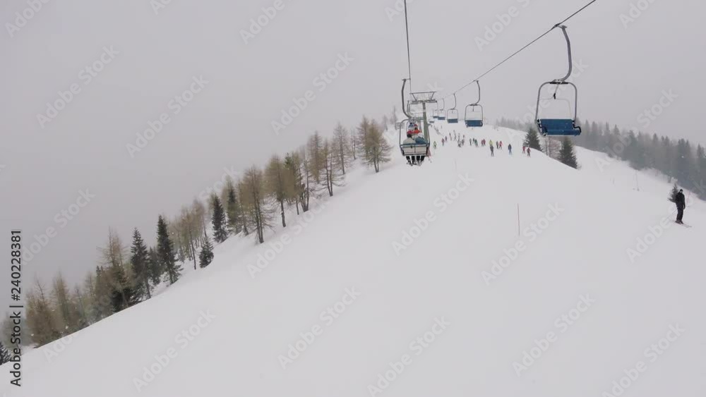 Going up on a chair lift under snowfall in mountains above ski tracks Going up on a chair lift under snowfall in mountains above ski tracks