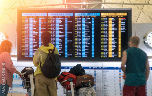 People in international airport looking at the flight information board, checking their flights. Tourists at international airport terminal flight timetable. Travel concept.