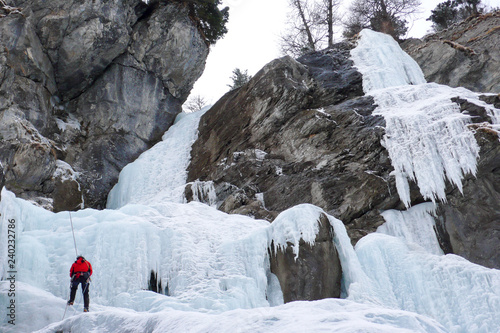 male ice climber rappelling off a steep frozen waterfall in winter photo