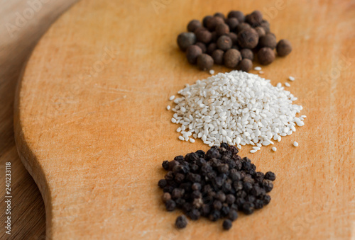 three handfuls of different spices (sesame, peppercorn, black pepper) on a wooden board in a row photo