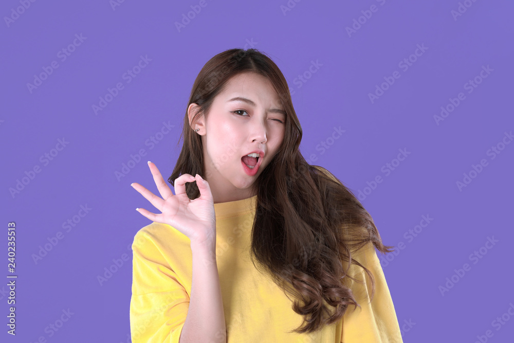 Fototapeta premium Asian woman accept deal with hand symbol, yellow t-shirt clothing, purple background