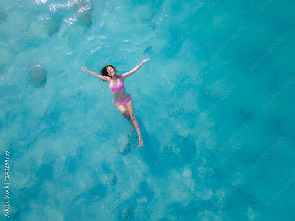 Aerial top view of young woman playing active swimming alone in the cleared water midsea, enjoy swimming im the sea of island tropical summer holiday