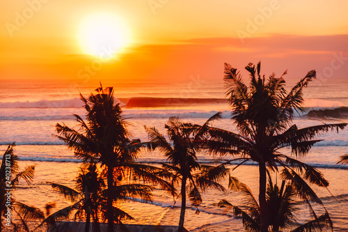 Warm sunset or sunrise with ideal ocean waves for surfing and coconut palms