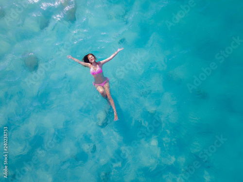 Aerial top view of young woman playing active swimming alone in the cleared water midsea, enjoy swimming im the sea of island tropical summer holiday
