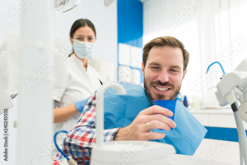 Attractive young man smiling at the dentist office  getting teeth repair  dental implants and teeth whitening by female dentist in a modern dental clinic. Male patient smiling in dentist chair.