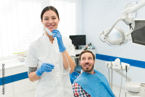 Happy young attractive female dentist with male patient in modern dental clinic smiling and wearing surgical gloves and mask. Medical and dentistry concept.