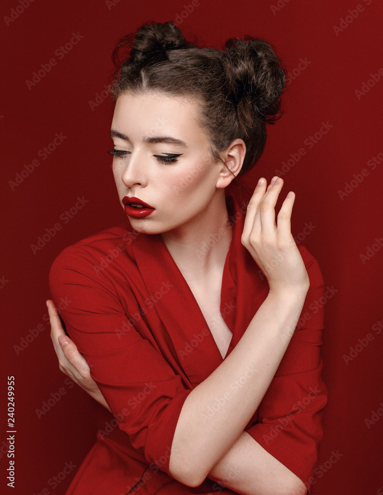 Brunette young woman with red lips wearing red dress on red background. Girl is posing in studio for Valentines day greeting card. Brunette young woman with red lips wearing red dress on red background. Girl is posing in studio for Valentines day greeting card.