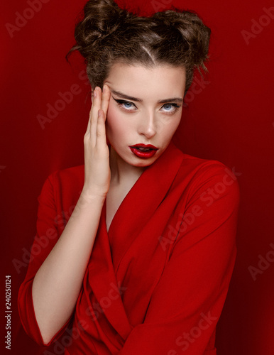 Brunette young woman with red lips wearing red dress on red background. Girl is posing in studio for Valentines day greeting card.