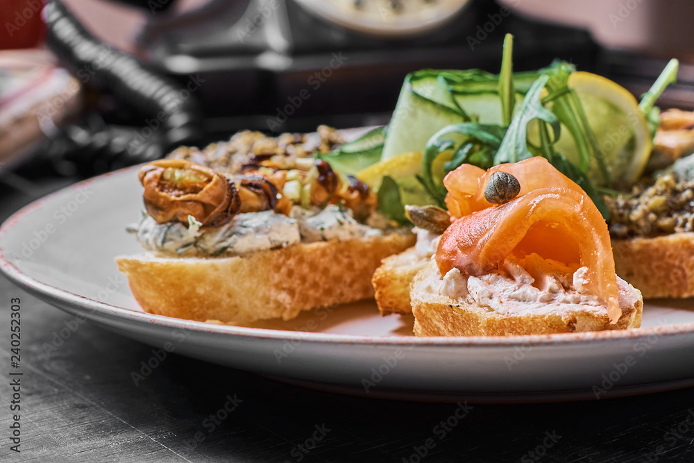 Tasty various italian sandwiches with seafood against rustic wooden background. Crostini with cheese, red fish, lemon and sliced olives, horizontal view with selective focus