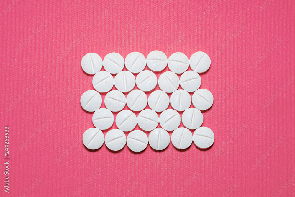 Lots of white smooth convex tablets with dividing strip on pink striped background, rectangle shaped, top view Lots of white smooth convex tablets with dividing strip on pink striped background, rectangle shaped, top view