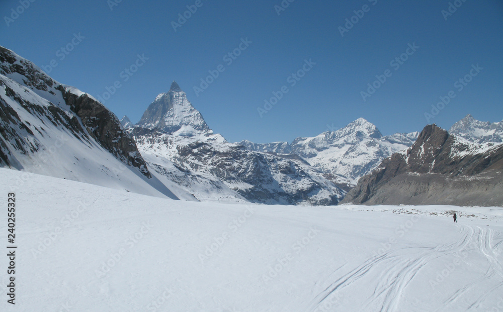 the Monte Rosa mountain range and Matterhorn mountain peak in the Swiss Alps above Zermatt in winter with a backcountry skier in the foreground