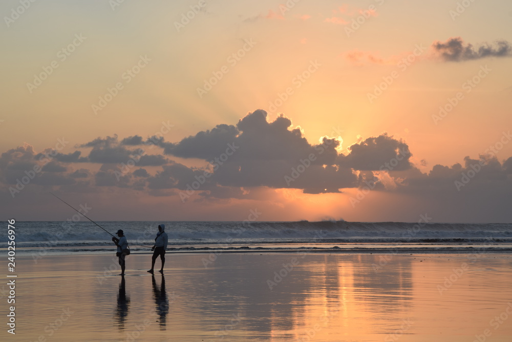 Fishing men on beach during sunset