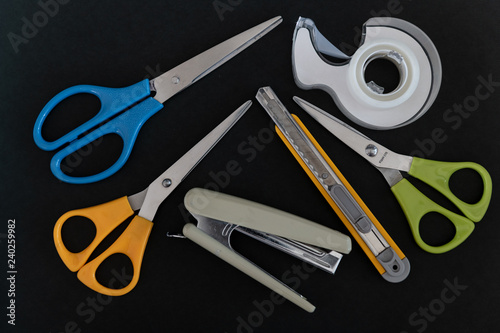 Stationery set with scissors, pen cutter knife, tape dispenser and stapler on black background