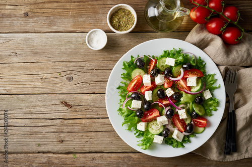 Greek salad on white plate on old rustic wooden table, top view, copy space