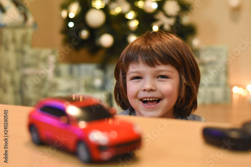 Happy boy play with car toys for Christmas. Smiling child having fun and playing with cars. Colorful lights on background