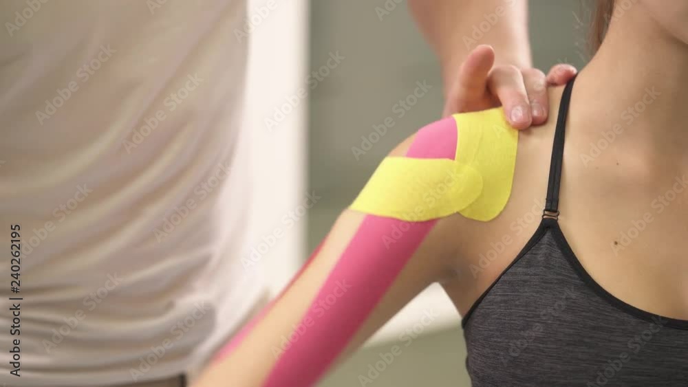 A male physiotherapist rises up and down, turns twice a woman's arm with applied kinesiotape. A functional test for a shoulder joint