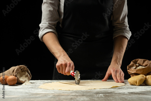 The chef cuts Italian pasta from dough. Against a dark background. A concept of preparing delicious food, Italian cuisine and recipes. Horizontal photo