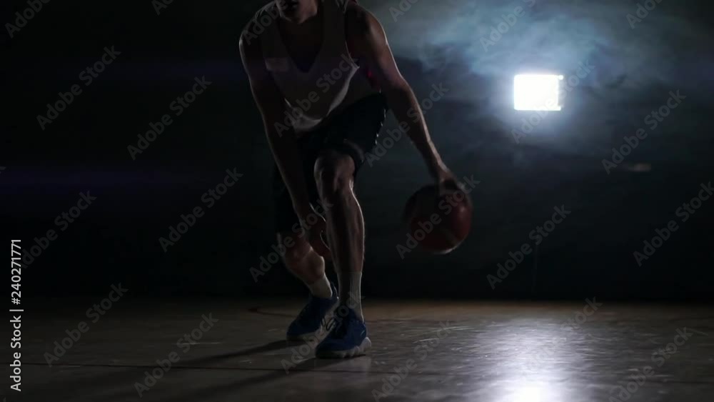 one young adult man, basketball player dribble ball, dark indoors basketball court. Smoke slow motion