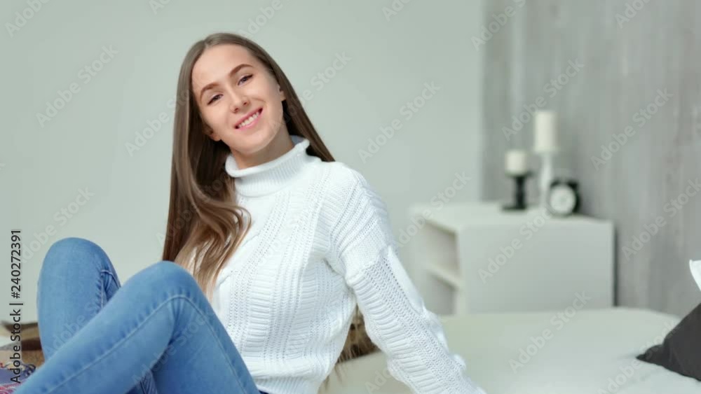 Medium long shot charming young woman smiling sitting on bed in modern bedroom Medium long shot charming young woman smiling sitting on bed in modern bedroom