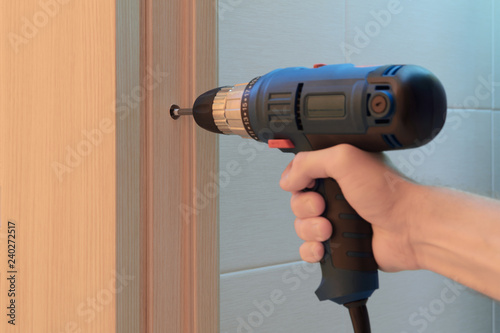 worker's hand with a screwdriver twists the screw and sets the door