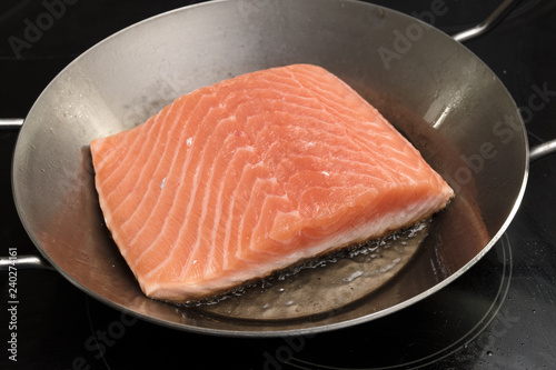 fresh salmon fillet is fried in an iron pan on the stove