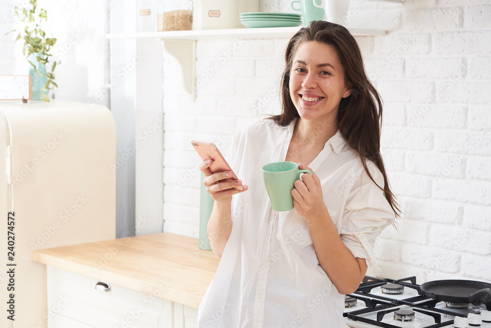 Young woman using smartphone leaning at kitchen table with coffee mug and organizer in a modern home. Smiling woman reading phone message. Brunette happy girl typing a text message.
Young woman using smartphone leaning at kitchen table with coffee mug and organizer in a modern home. Smiling woman reading phone message. Brunette happy girl typing a text message.
