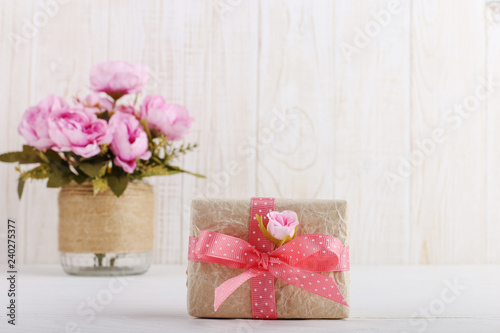 Pink flowers in a vase and a gift in craft paper on the table. Concept of Women's Day or St. Valentine.