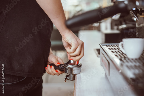 Barista presses ground coffee using tamper. Close-up view on hands