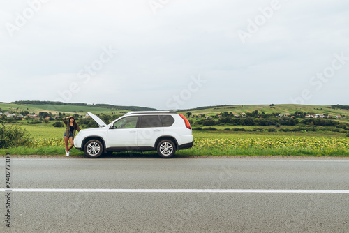 woman stand at roadside near broken car with opened hood