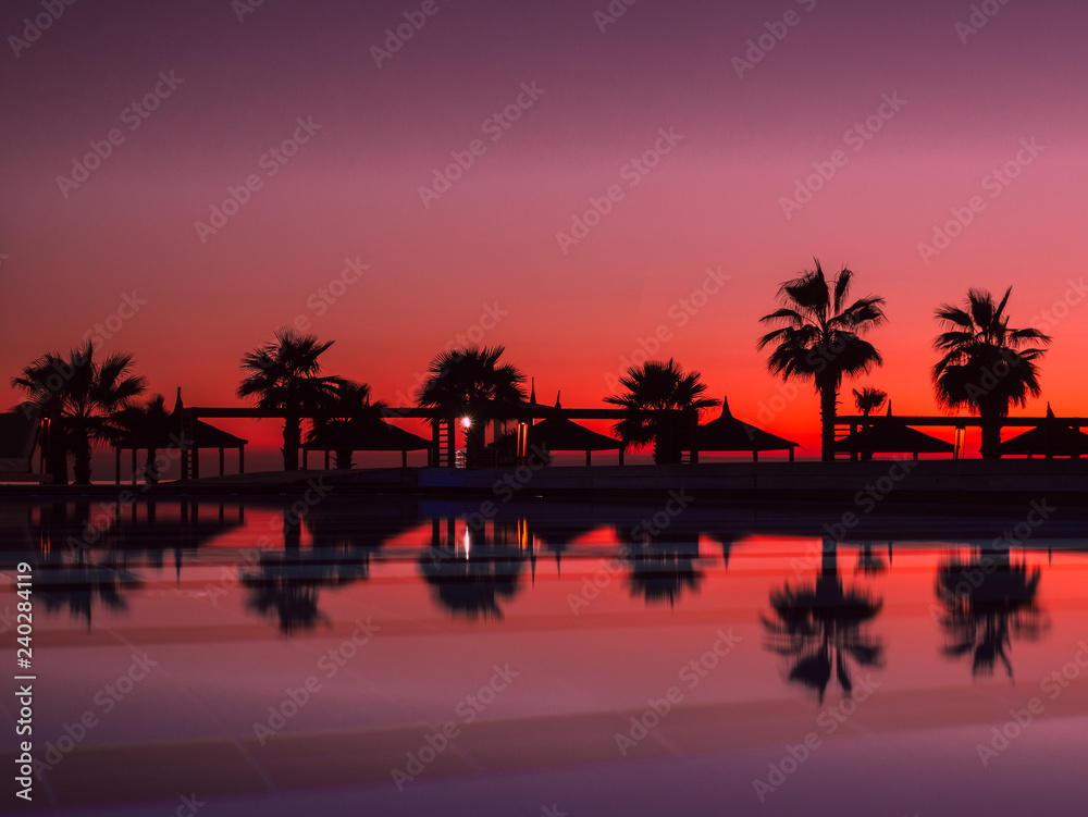 Sunset with silhuettes palm and reflection in swimming pool	