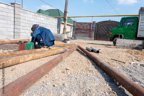 worker welds a rusty pipe in the street in the yard of the plant