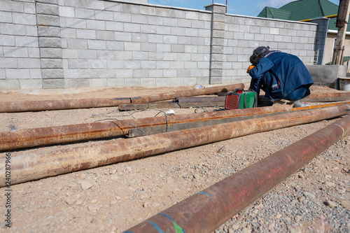worker welds a rusty pipe in the street in the yard of the plant