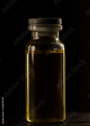 small medical Bottle, with yellow inside, on a black background, close-up,