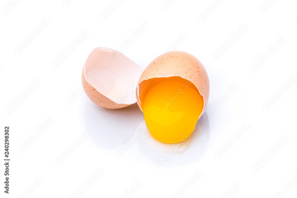 A broken brown organic egg with egg yolk on a white background. A broken brown organic egg with egg yolk on a white background.