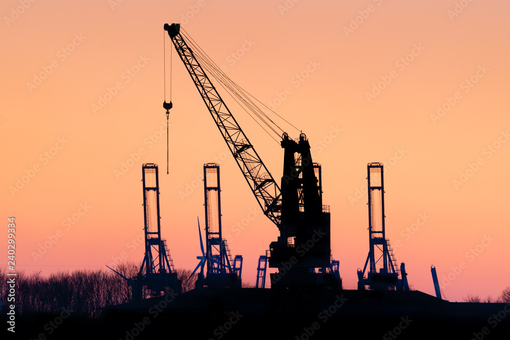 Cranes silhouetted against the evening sky in Hamburg Harbor, Germany, at dusk. The Port of Hamburg (Hamburger Hafen) is a sea port on the river Elbe. It is Germany's largest port.