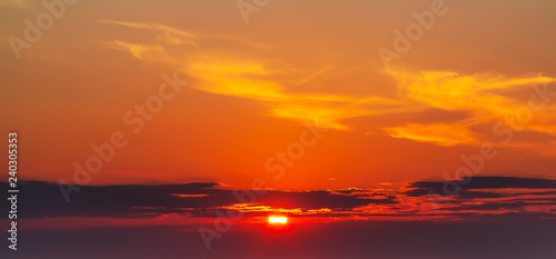 sky during a colorful, bright orange sunset, sun's rays make their way through the clouds