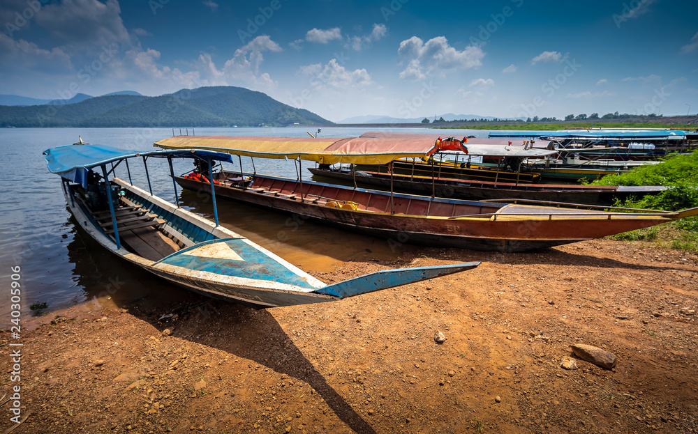 Many long trail boats are parked at the river side, with the island behind in Thailand.