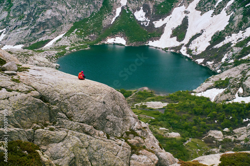 Tourist sitting on the rock high above the big mountain lake in Corsica mountains GR20