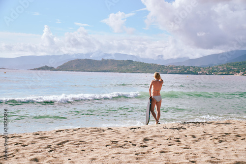 Surfer girl standing on a sand beach and watching the waves on sunny day in Corsica