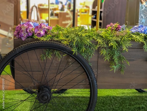 Wooden flower cart or carriage decoration on black colored spoked bicycle wheels