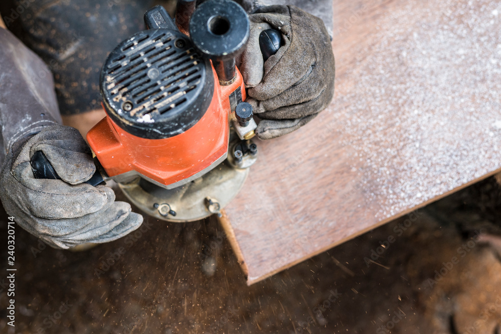 Hand of carpenter using electric planer with wooden plank
