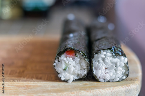 Making Sushi Rolls at Home: Two Shaped Round Rolls Sealing on a Wooden Board before Slicing. Blurred Kitchen Table in Background. photo