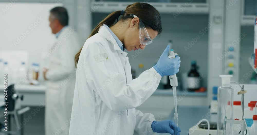 Portrait of female scientist with a pipette analyzes a liquid to extract the DNA and molecules in the test tubes in laboratory. Shot in 8K. Concept: research,biochemistry, pharmaceutical medicine Portrait of female scientist with a pipette analyzes a liquid to extract the DNA and molecules in the test tubes in laboratory. Shot in 8K. Concept: research,biochemistry, pharmaceutical medicine