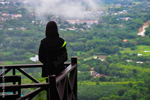 Women stand facing the view on a wooden balcony. It has a natural background and fog. Phu Bo Bit, Loei, Thailand.