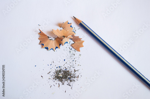 A pencil sharpened with pencil peels and black graphite lead waste on a white background