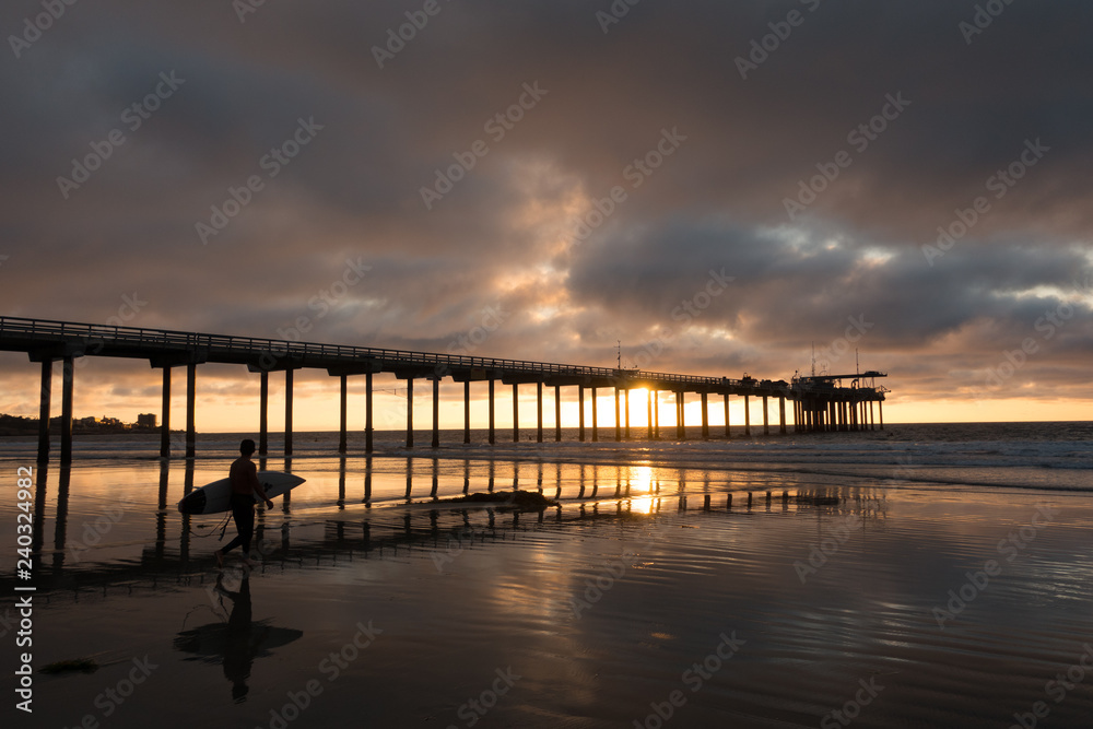 Silhouette of a surfer walking on the beach under the Scripps Pier in San Diego California
