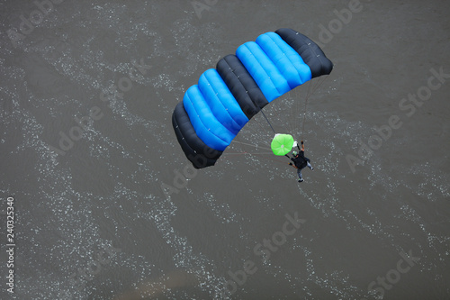 Base jumper under the canopy of a parachute in the background of the water surface. View from above.