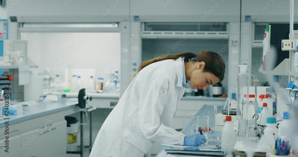 Portrait of female scientist make analysis of the DNA and molecules in the test tubes and signs results in laboratory. Shot in 8K. Concept: research,biochemistry, pharmaceutical medicine Portrait of female scientist make analysis of the DNA and molecules in the test tubes and signs results in laboratory. Shot in 8K. Concept: research,biochemistry, pharmaceutical medicine