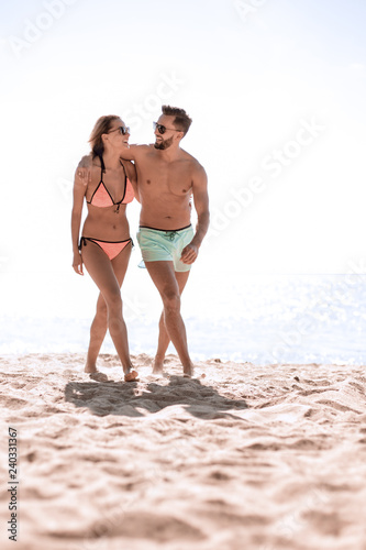 Young couple holding hands and walking on beach.