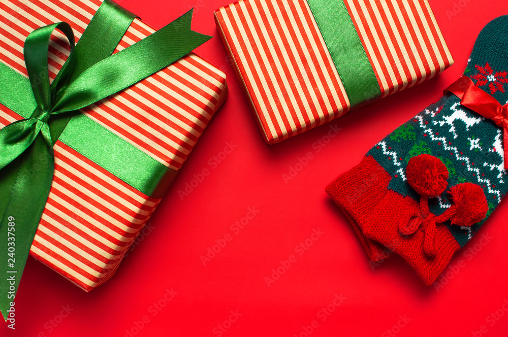 Fototapeta premium Woolen socks with a Christmas New Year ornament and gift box on red background top view flat lay. Holiday concept, presents Xmas. Congratulations background with space for text.